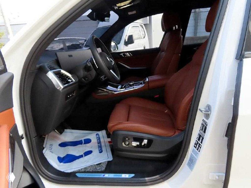 Переднее пассажирское место BMW X7 с открытой дверью, коричневая кожаная отделка сидений и вид на панель и порог автомобиля