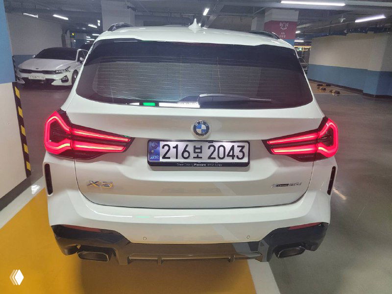 Прямой вид сзади белого BMW X3 xDrive 20i MSport: задние фонари, бампер и номерный знак видны чётко в освещении паркинга.