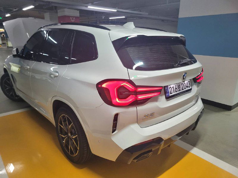 Задний правый ракурс BMW X3 xDrive 20i MSport в белом цвете, виден контур багажника и боковая часть кузова на парковочном месте.