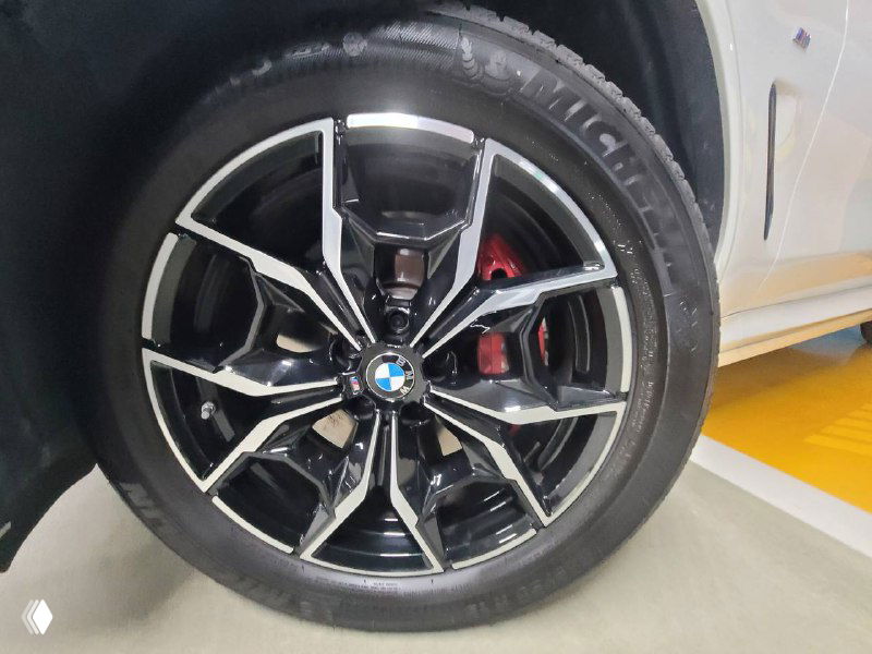 Крупный план диска и тормозного суппорта BMW X3 xDrive 20i MSport, чёрно-серый легкосплавный диск с красным суппортом в паркинге.