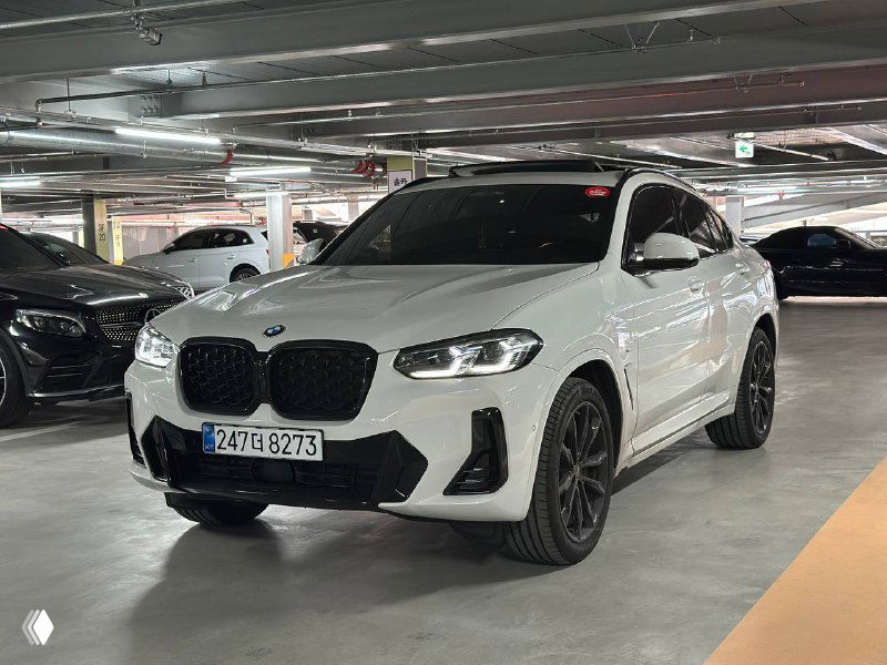 Общий трёхчетвертной ракурс белого BMW X4 xDrive — чёрные диски, профиль кузова и контекст парковки в гаражном комплексе.