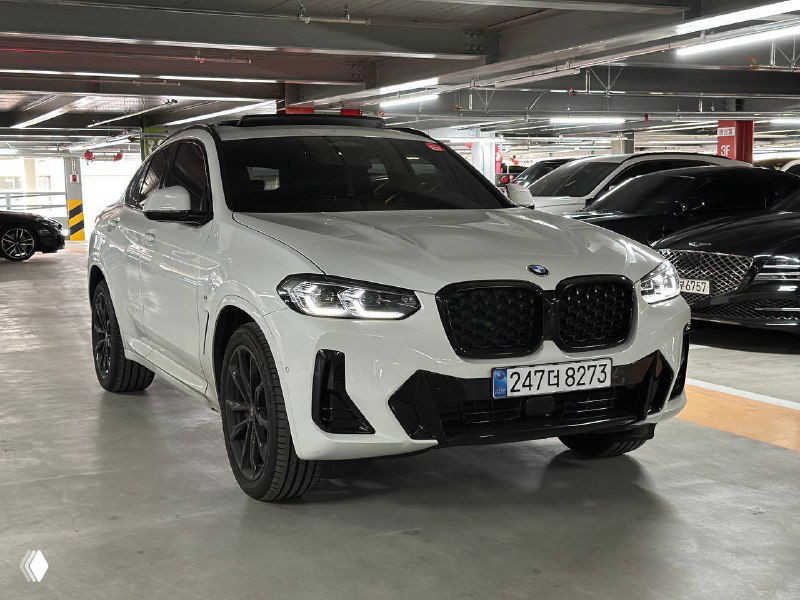 Белый BMW X4 xDrive снят под углом спереди, подчёркнуты острые линии бампера, воздухозаборники и посадка автомобиля на стоянке.