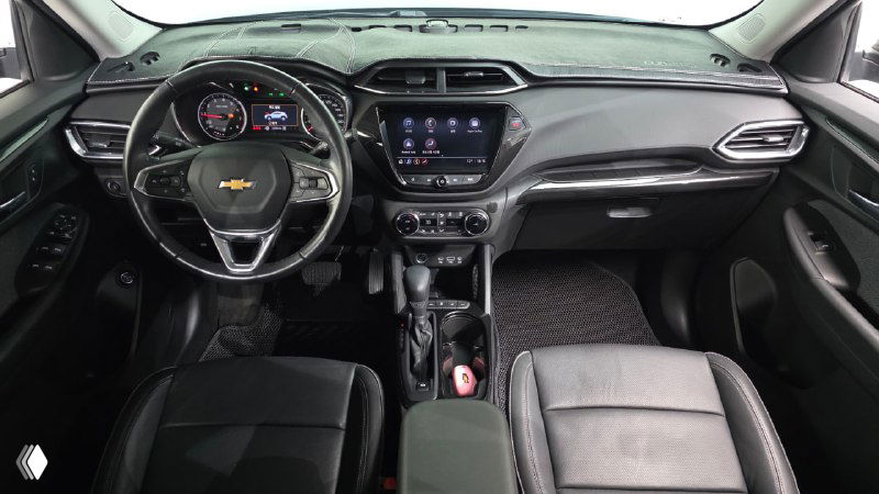Салон Chevrolet Trailblazer: общий ракурс приборной панели, руль, мультимедийный экран и передние сиденья, чёрная обшивка и детали интерьера.