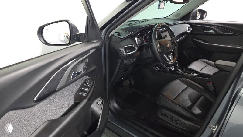 Вид с открытой передней дверью на водительское место Chevrolet Trailblazer, видны панель двери, руль, кресло и элементы управления с левой стороны.