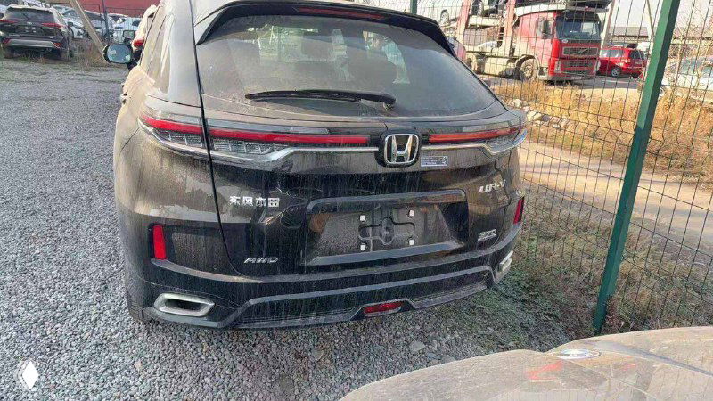 Задняя часть Honda UR-V 2025 на площадке: вид на фонарь, багажник, эмблему Honda и задний бампер без номерного знака, припаркованный у ограды.