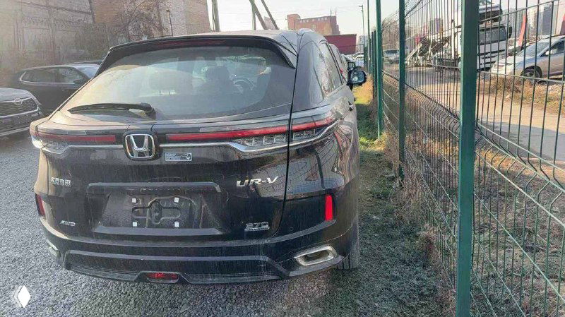 Угол сзади Honda UR-V 2025 — вид на багажник и левую часть заднего бампера, автомобиль на открытой стоянке возле других машин.