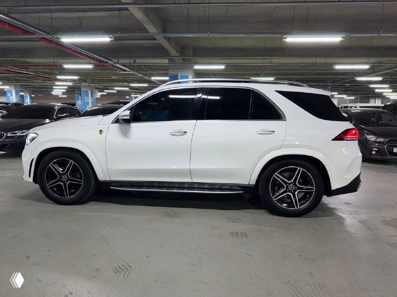 Боковой профиль белого Mercedes GLE 300D в паркинге: вид со стороны пассажирской двери, чёрные элементы внизу и легкосплавные диски.