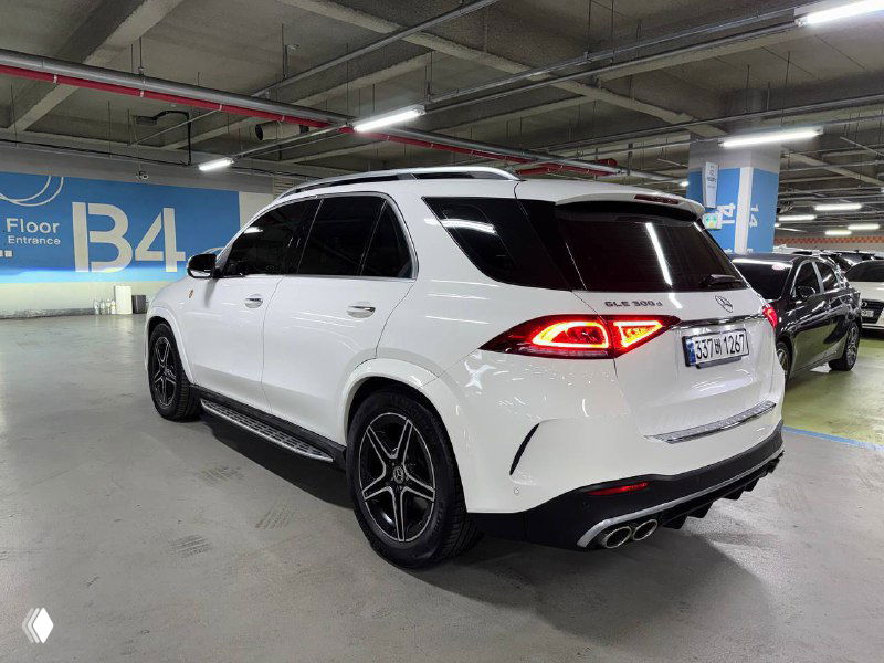 Вид сзади и под углом белого Mercedes GLE 300D: задняя оптика, выхлопные патрубки и общая линия багажника в закрытом паркинге.