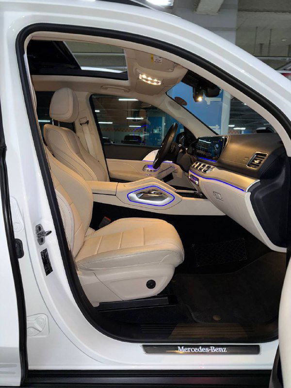 Открытая передняя дверца и вид на переднее пассажирское сиденье белого Mercedes GLE 300D: светлая кожаная обивка и фирменная подсветка салона.