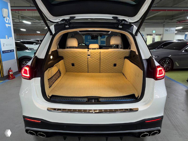 Открытый багажник белого Mercedes GLE 300D с ковриком и ровным пространством для груза: вид сзади в паркинге на приёме освещения.