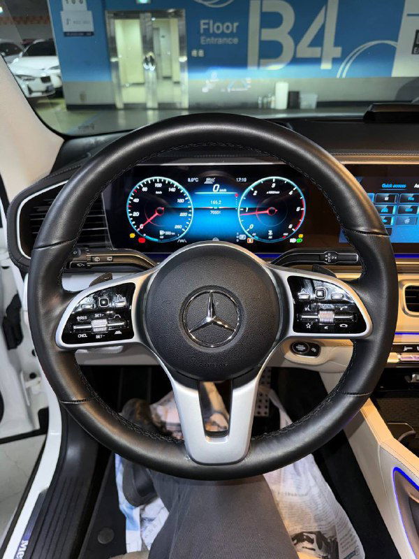 Вид на руль и приборную панель Mercedes GLE 300D: круглый руль с логотипом, цифровые указатели скорости и стильные кнопки управления на ободе.