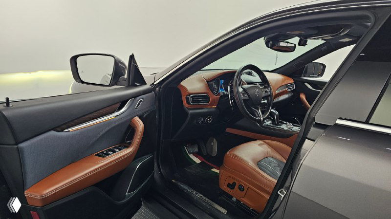 Открытая дверная группа и вид на водительское сиденье Maserati Levante с контрастной коричневой кожей и декоративной строчкой.