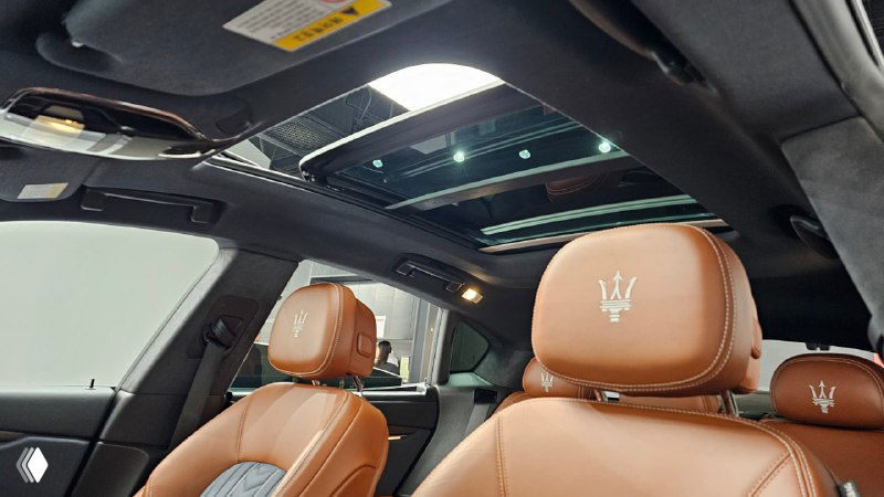 Панорамная крыша и задняя часть передних сидений Maserati Levante, видна вышивка с логотипом на подголовниках и стеклянная крыша.
