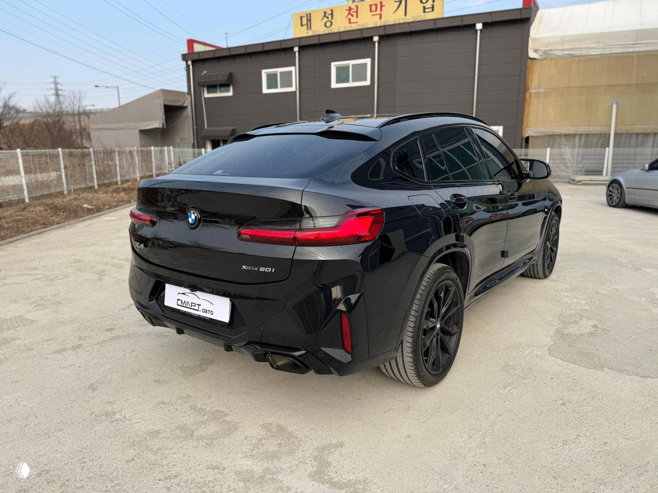 Вид сзади‑слева чёрного BMW X4: купеобразная линия крыши, задние фонари и спортивный бампер с двойными патрубками выхлопа.