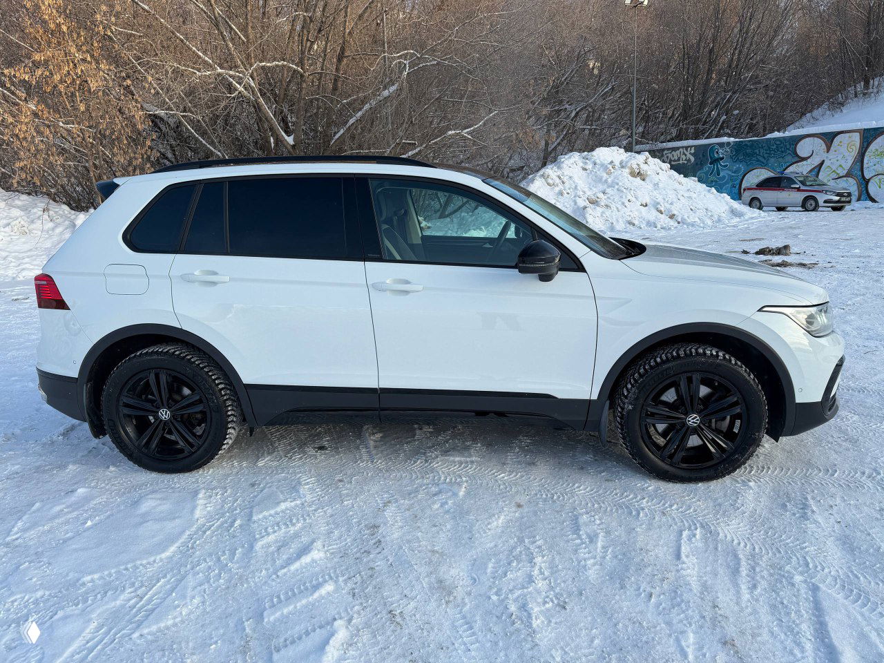 Боковой профиль белого Volkswagen Tiguan 2022 на снегу, заметны тонированные задние стёкла и чёрные молдинги.