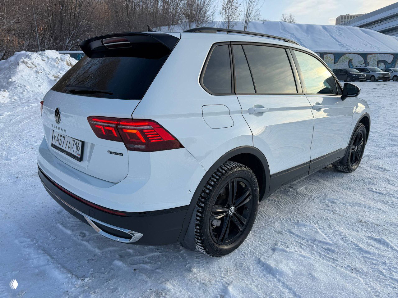 Задний угол Volkswagen Tiguan Urban Sport: белый кузов, задние фонари и интегрированный спойлер, чёрные диски на фоне снега.