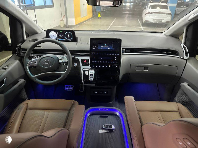 Широкий план салона Hyundai Staria с подсветкой пола, центральной панелью и двумя рядами сидений, подчёркивающий интерьер и пространство для пассажиров.