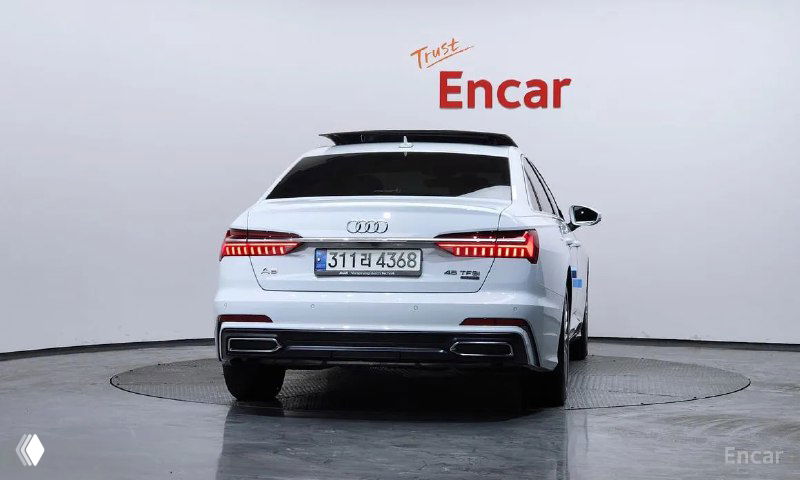 Задняя часть белого Audi A6 2020 года, видны светодиодные фонари, бампер и номерной знак на студийном фоне поворотной платформы.