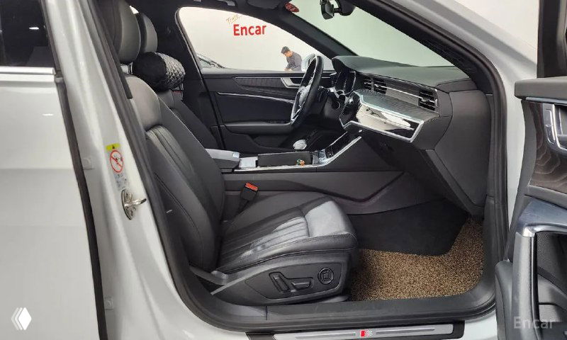 Переднее пассажирское сиденье Audi A6 с открытой дверью, чёрная кожаная обивка, декоративные вставки и напольный коврик в салоне.