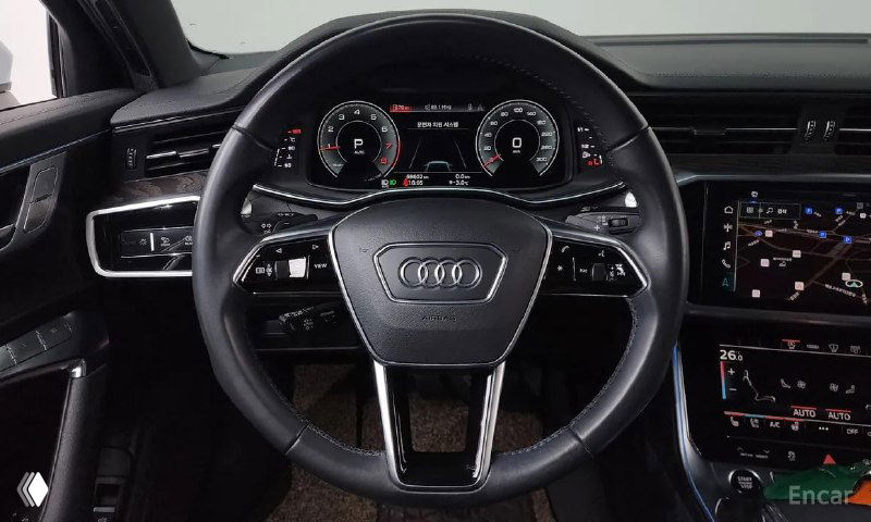 Рулевое колесо Audi с логотипом и вид на цифровую приборную панель, мультимедийные элементы управления и часть центральной консоли.