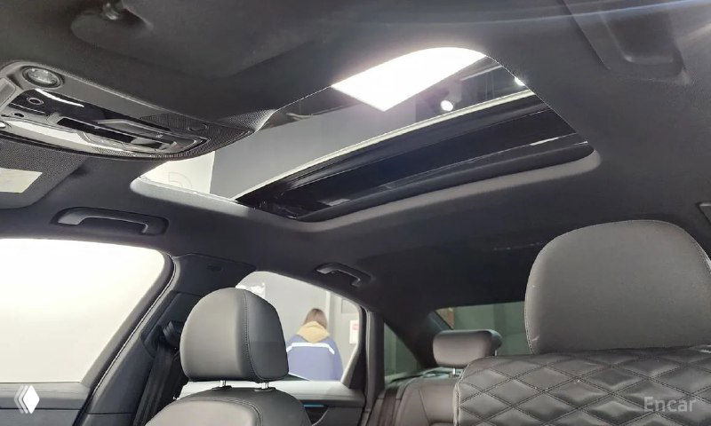 Панорамный люк в крыше автомобиля Audi A6, вид на стеклянную секцию люка и обивку потолка салона с передними сиденьями в кадре.