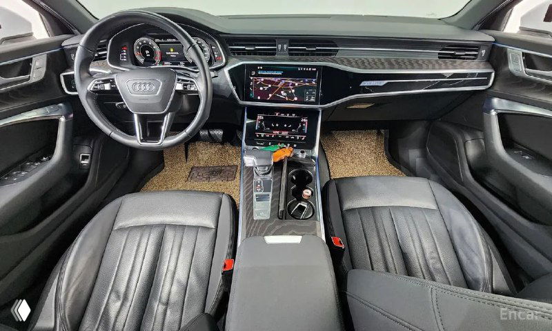 Вид из салона на передние кресла и центральную консоль Audi A6 с включёнными мультимедийными экранами и декоративными вставками.