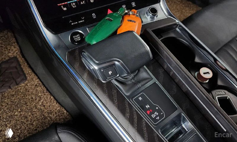 Крупный план селектора передач и центральной консоли Audi A6: кожаная отделка, органы управления и подстаканники вблизи.