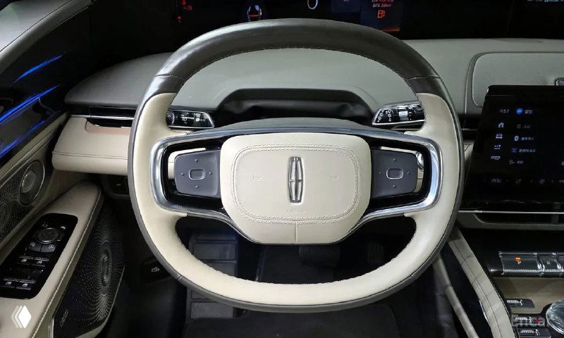 Руль Lincoln Nautilus 2023 крупным планом: кожаная отделка, кнопки на руле и логотип бренда в центре, видно дизайн салона вокруг.