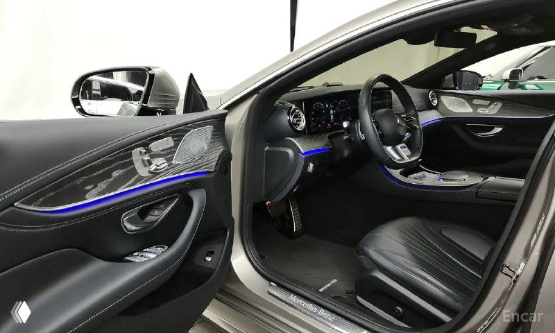 Открытая водительская дверь и вид на переднее сиденье Mercedes‑Benz CLS450 с подсветкой, видно отделку дверной карты и элементы управления.