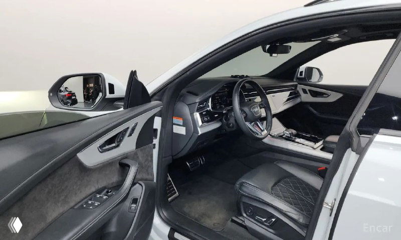 Вид на водительскую дверь и боковую панель Audi Q8: элементы управления, обивка дверей и зеркала на фоне открытой двери, пространство подходит для проверки.