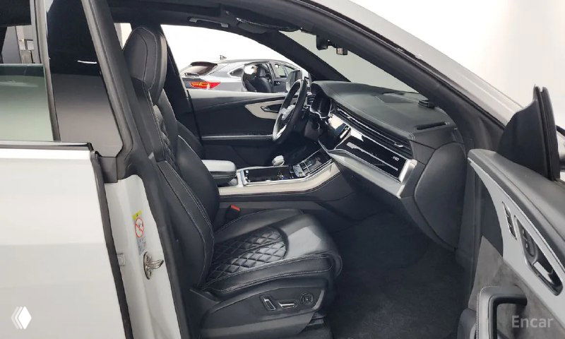 Передние сиденья Audi Q8 в кожаной отделке с ромбовидной прострочкой, хорошо видна общая сохранность салона и состояние подлокотника.