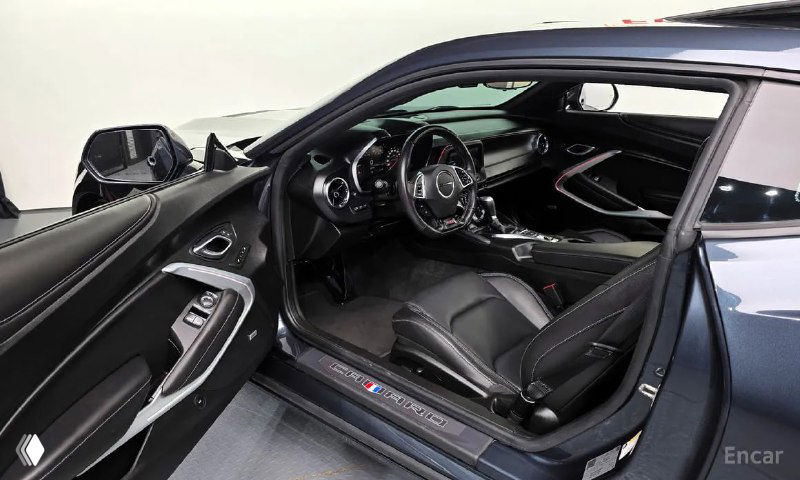 Интерьер Chevrolet Camaro SS 2021 — водительская дверь открыта, чёрная кожаная отделка сидений и часть приборной панели видна.