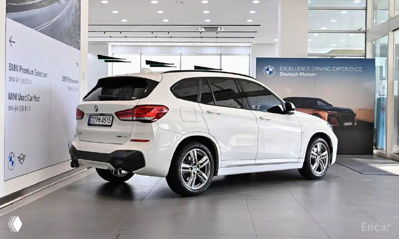 Задний и боковой профиль белого BMW X1 xDrive 20i M Sport в салоне дилера: подчёркнуты линии кузова и состояние лакокрасочного покрытия.