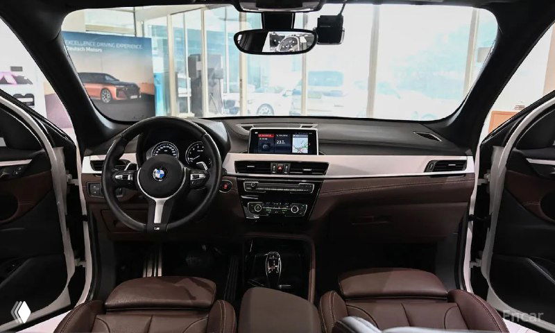 Интерьер BMW X1: общий вид на переднюю панель, руль, мультимедиа и чёрно-коричневую отделку салона в хорошем состоянии.