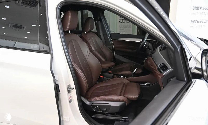 Вид на водительское кресло BMW X1 с открытой дверью: коричневая обивка, место водителя и панель управления в салоне дилера.