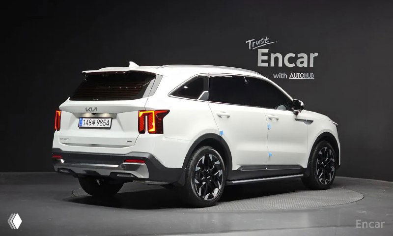 Задний ракурс белого Kia Sorento в студии, видно форму багажника и задние фонари на фоне нейтральной стенки с логотипом.