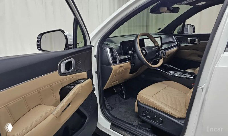 Открытая дверь водителя и вид на рулевое колесо и передние сиденья бежевого цвета, зоны входа и обивка двери в светлых тонах.