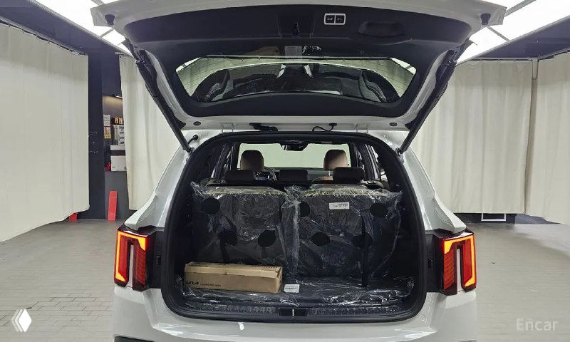 Открытый багажник белого Kia Sorento, вид сзади внутрь грузовой зоны, в ней упаковочные материалы и ровный пол багажника.