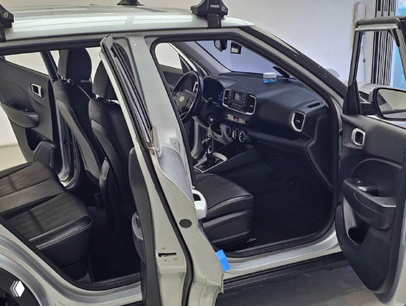 Открытые передние и задние двери Hyundai Venue, чёрный салон, вид на передние и задние сиденья и рулевую колонку — фото интерьера для объявления.