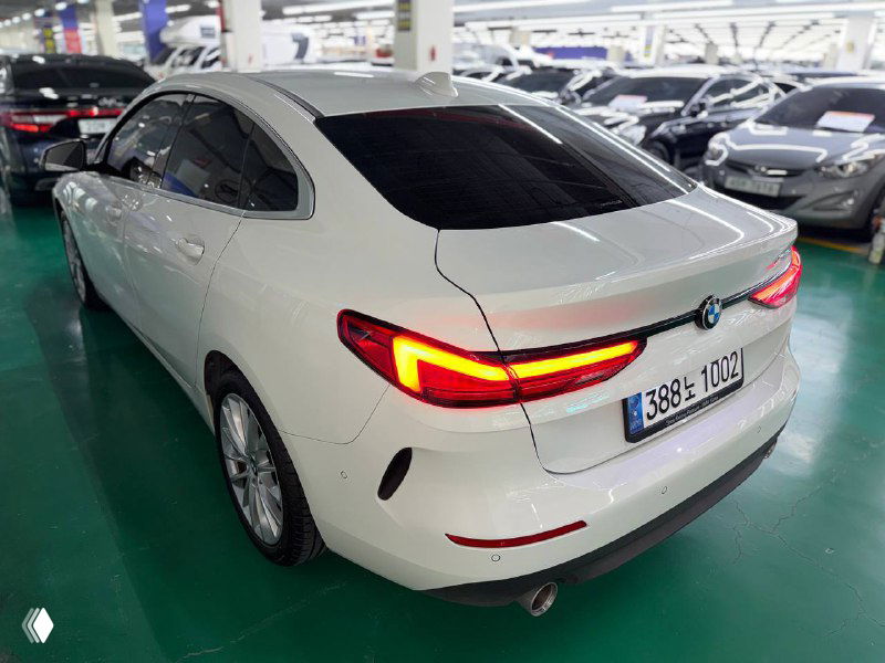 Задняя часть белого BMW 218D Advantage 2020 с включёнными задними фонарями, осмотр багажника и кормы на стоянке салона