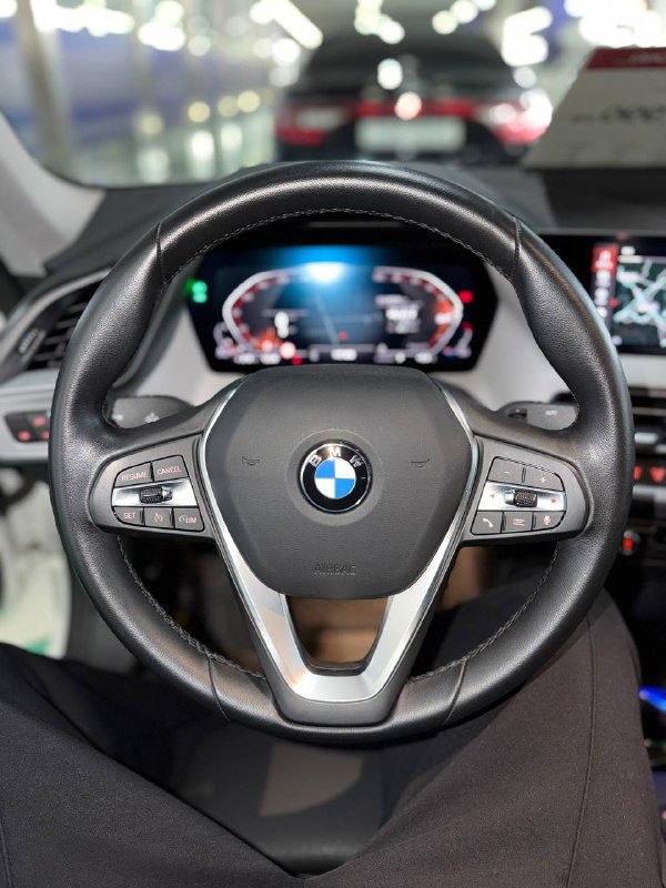 Крупный план рулевого колеса BMW с логотипом, кнопки управления на руле, вид в салоне автосалона на демонстрационном экземпляре