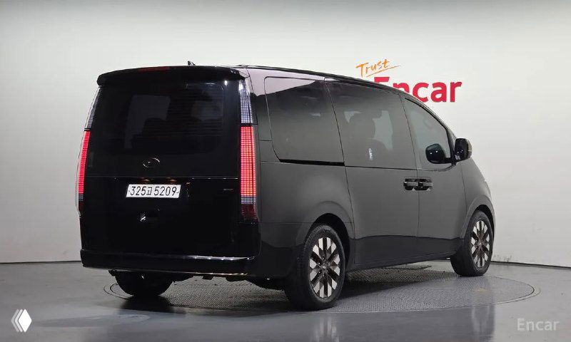 Hyundai Staria 2023 — вид сзади в шоуруме: задняя часть минивэна, вертикальные фонари и закрытая задняя дверь на светлом фоне стенда.