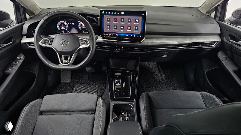 Панорамный вид на переднюю панель и мультимедийный экран Volkswagen Golf, чистый современный интерьер и руль слева.