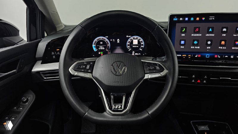 Крупный план рулевого колеса Volkswagen Golf с элементами управления и цифровой приборной панелью на фоне центральной консоли.