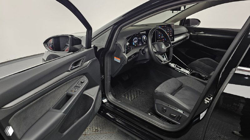 Открытая передняя водительская дверь, вид на сиденье и внутренние панели двери чёрного Volkswagen Golf в выставочном помещении.