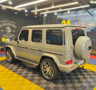 Задний ракурс Mercedes G63 AMG: запасное колесо на двери багажника, светодиодные фонари и общий вид автомобиля на показе.
