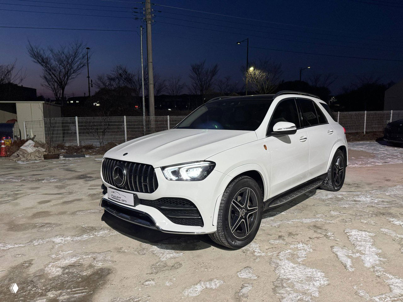 Угловой вид белого Mercedes GLE 300D 4Matic на стоянке ночью, видна боковая часть и дизайн колёс AMG.
