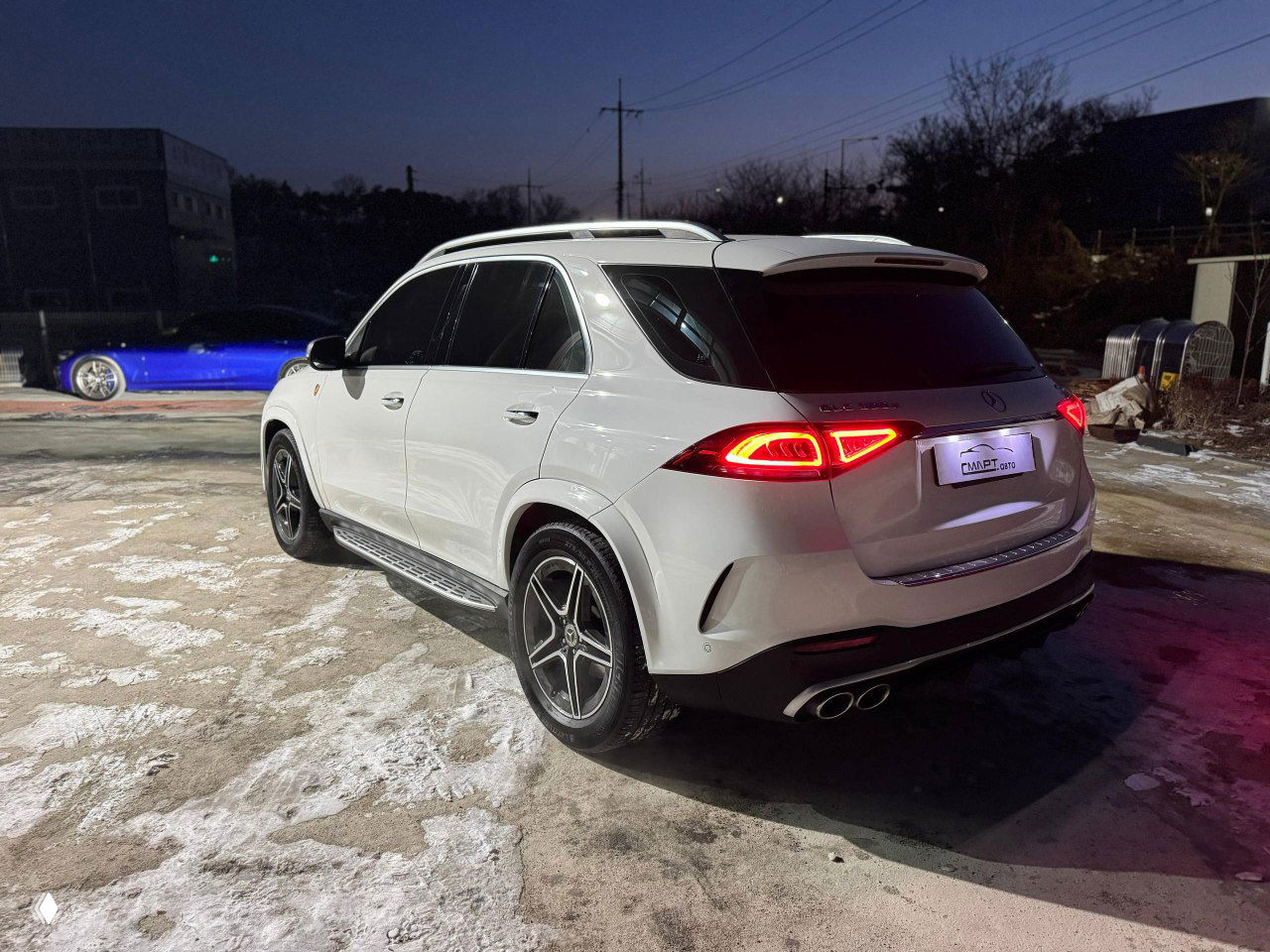 Вид сзади и в три четверти белого Mercedes GLE 300D, включённые задние фонари, выхлопные патрубки и багажник.