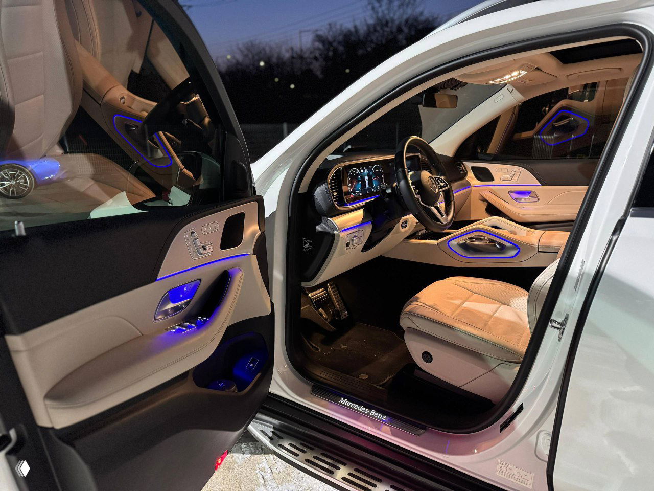 Открытая передняя пассажирская дверь и салон Mercedes GLE: бежевые сиденья и мягкая подсветка дверных панелей.