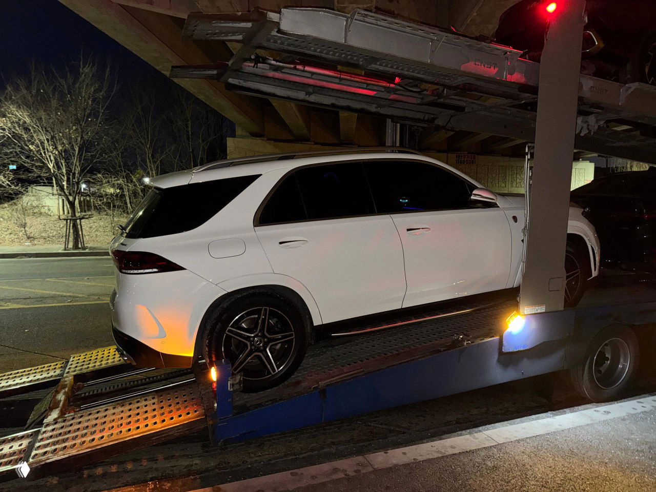 Белый Mercedes GLE в профиль на платформе автовоза ночью, вид на боковую часть и колёса во время подготовки к отправке